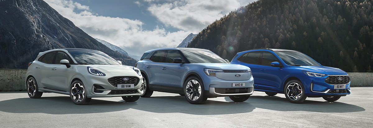 Drei Autos in den Farben Weiß, Blau und Silber stehen in einer Berglandschaft, umgeben von Bergen und Wolken.
